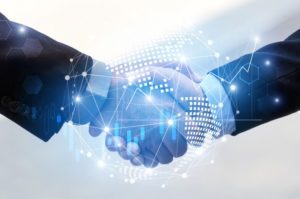 Two suited businessmen shaking hands, financial icons and stock market data superimposed over handshake