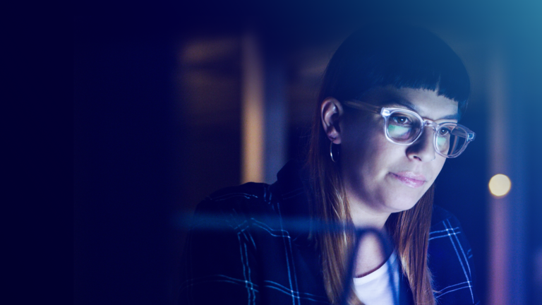 Female professional in glasses glancing at reflection of laptop screen in office environment