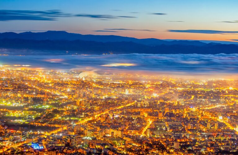 Sofia lit up at dusk with mist and mountains in the background