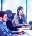 Professional team of people at work in office environment, sat in front of computers and typing on keyboards