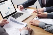 Financial executives in meeting, crowding around laptop to compare statistics