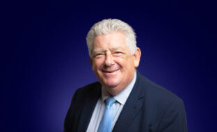 Ian Ganney, Chairman of the Board, a suited professional smiling towards the camera