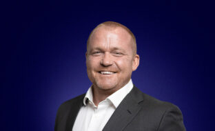 Desmond Stockdale, Founder and CEO a light haired man in a dark suit, smiles at the camera